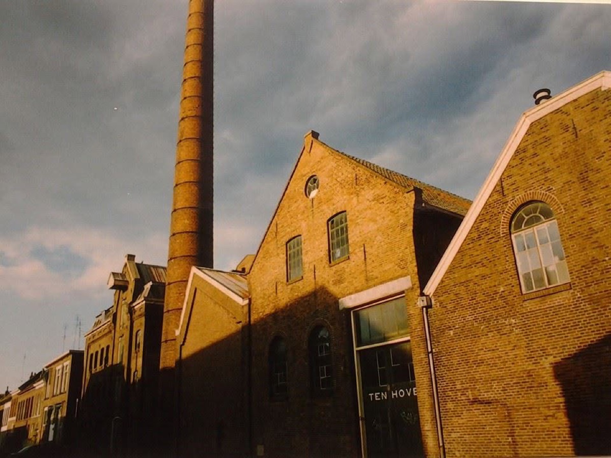Oude foto van de Ten Hove-fabriek met de hoge bakstenen schoorsteen in avondlicht